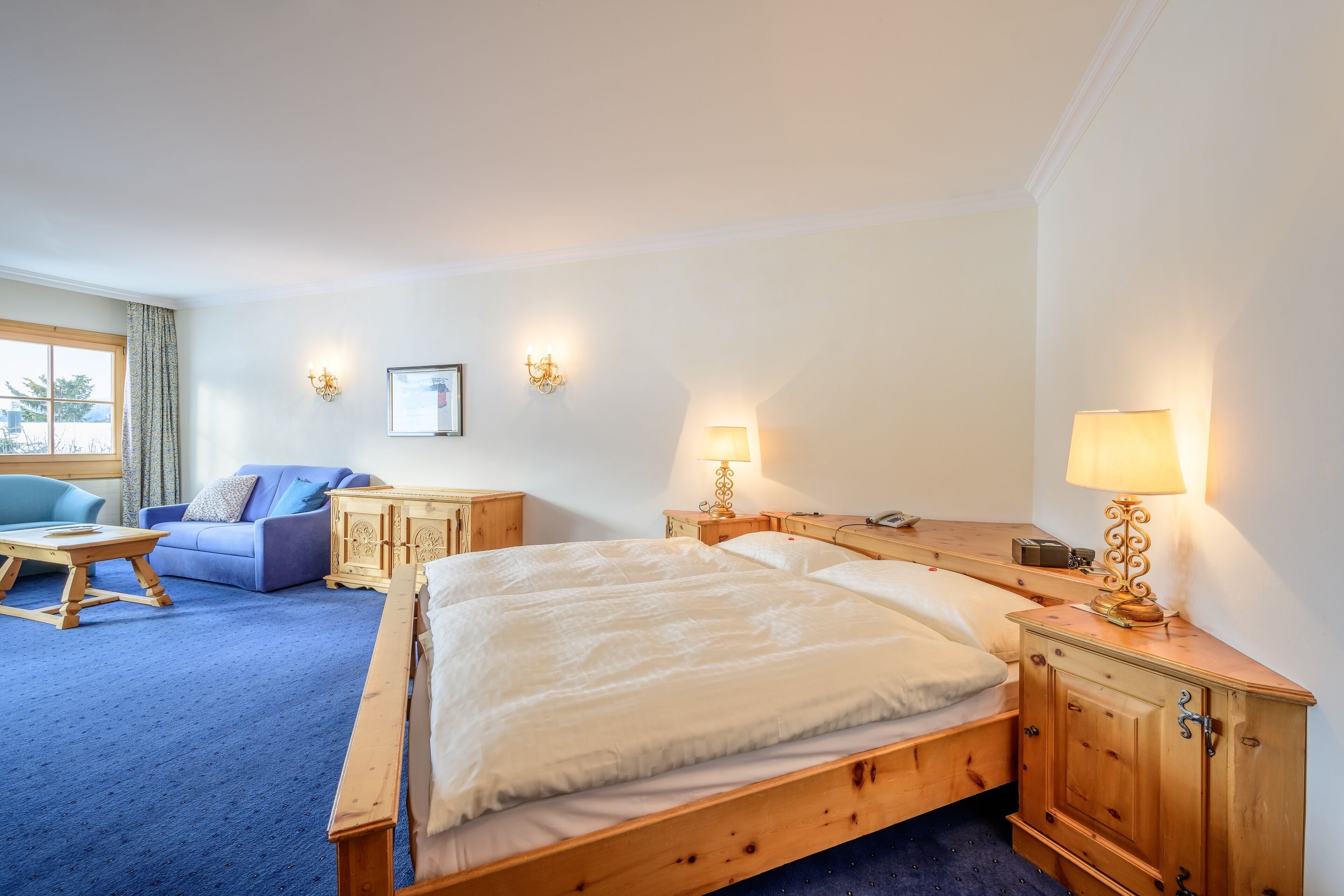 Una habitación de hotel con una cama grande, una mesita de noche de madera, una lámpara, un sofá y una ventana con cortinas.