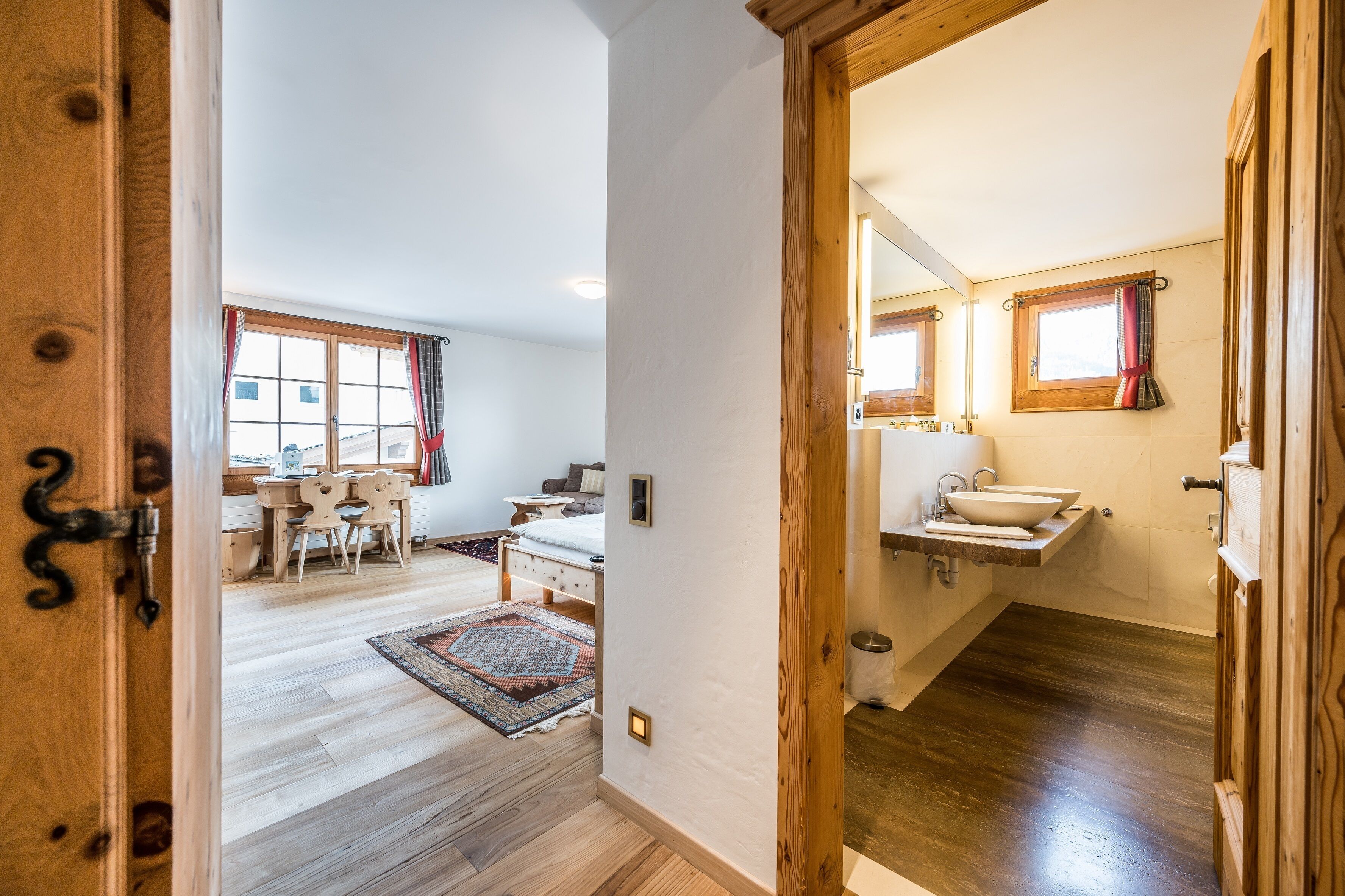 Une pièce avec un plancher en bois, un lit, un bureau et une fenêtre avec des rideaux.
