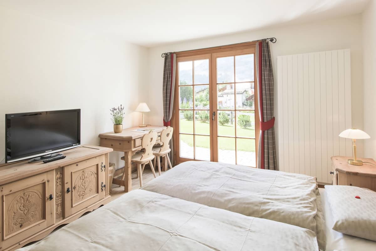 Habitación de hotel con dos camas, televisión, escritorio con silla y ventana con cortinas.