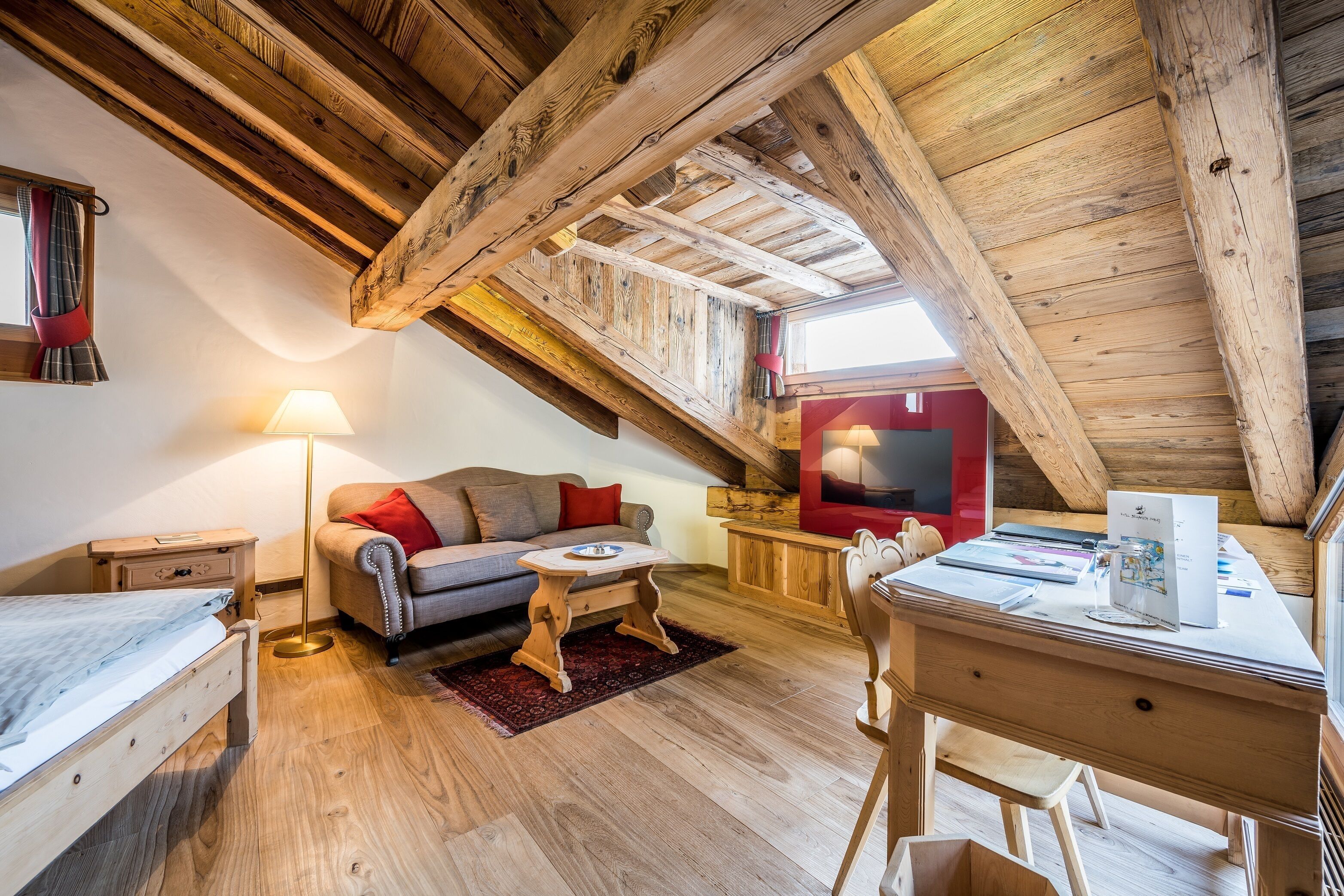 A cozy attic room with a loft bed, a sofa, a desk, and a lamp.