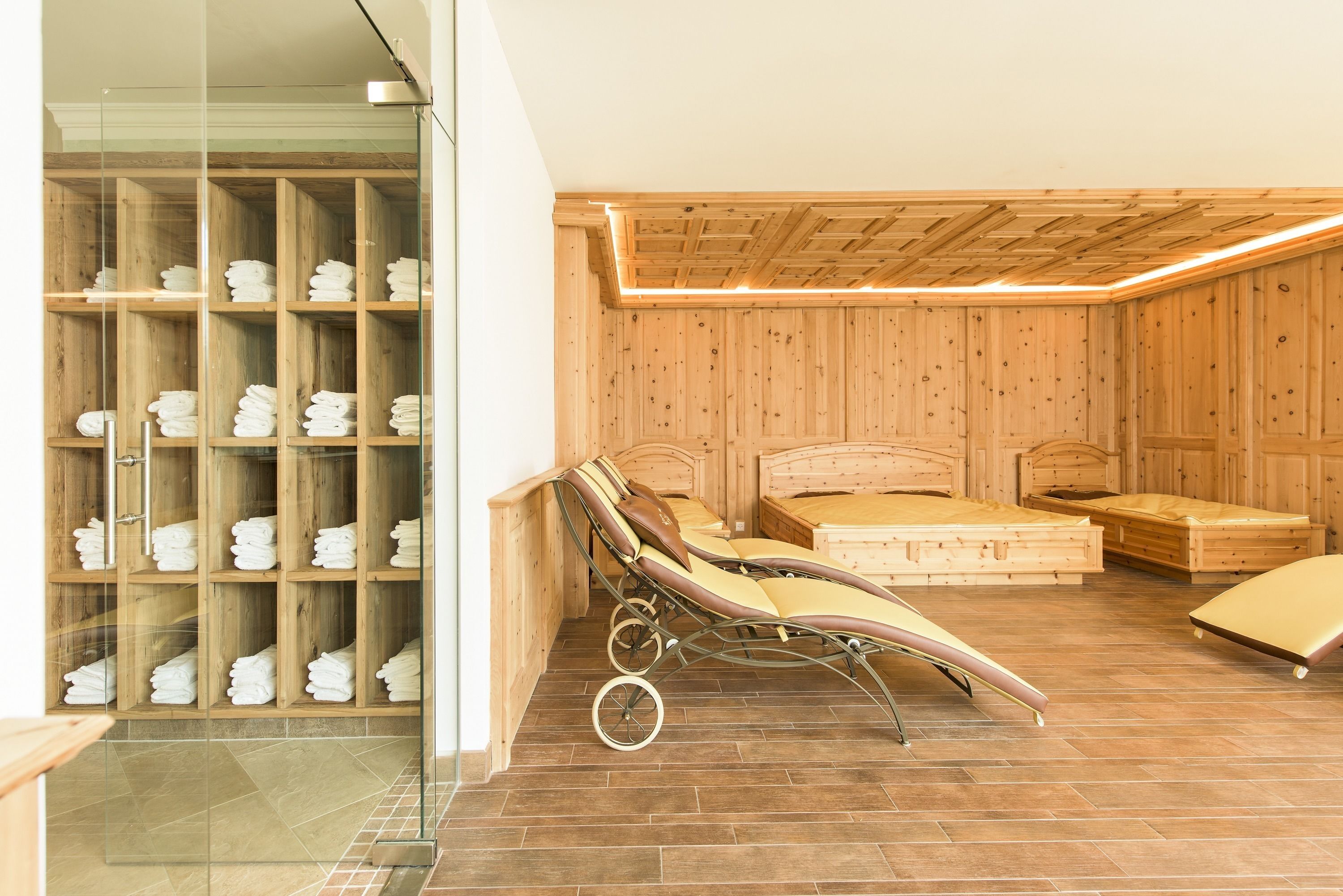 A wooden-paneled room with a glass shower enclosure, a bed with a headboard, and a bench.