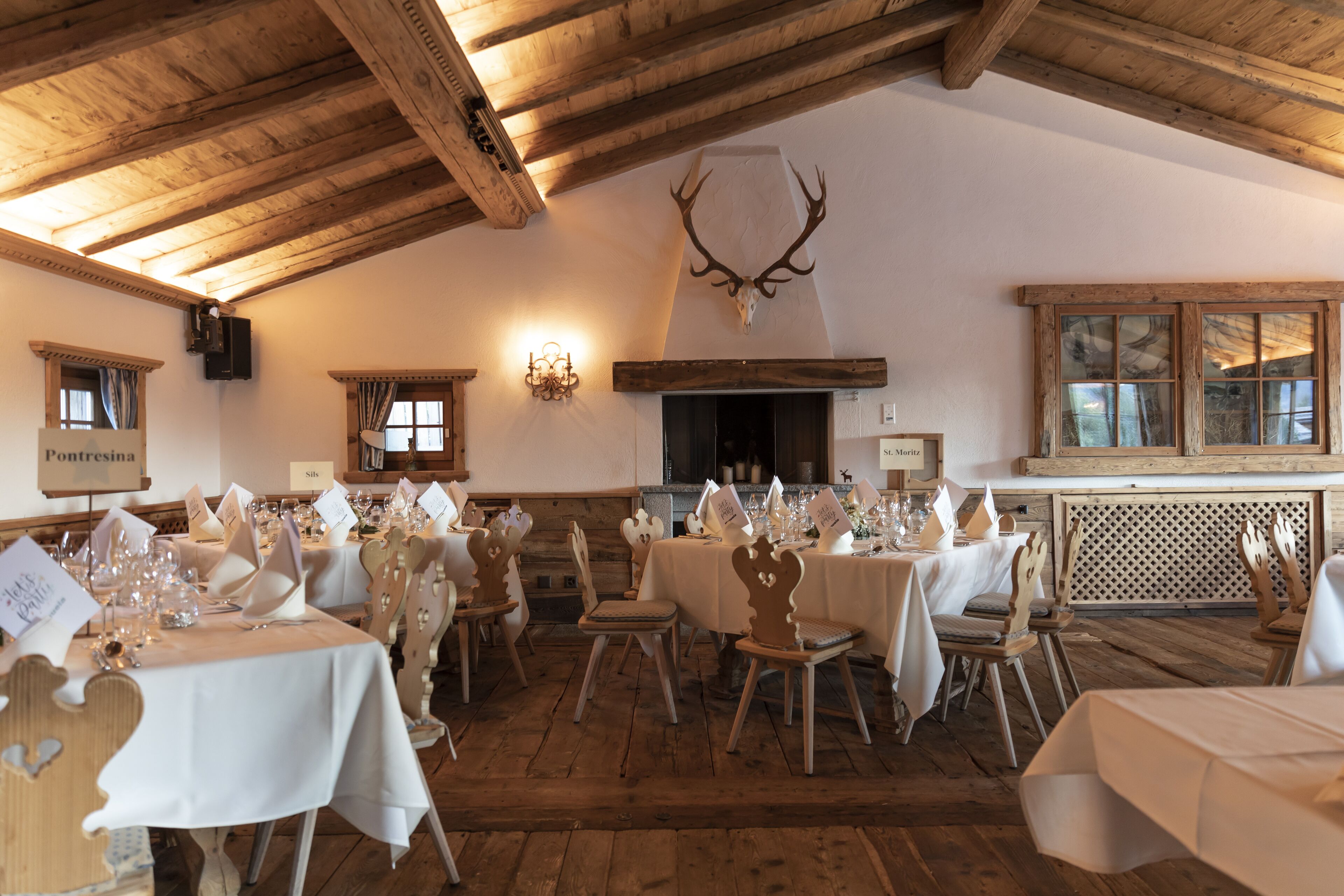 A dining area with wooden tables and chairs, a fireplace, and a deer skull on the wall.
