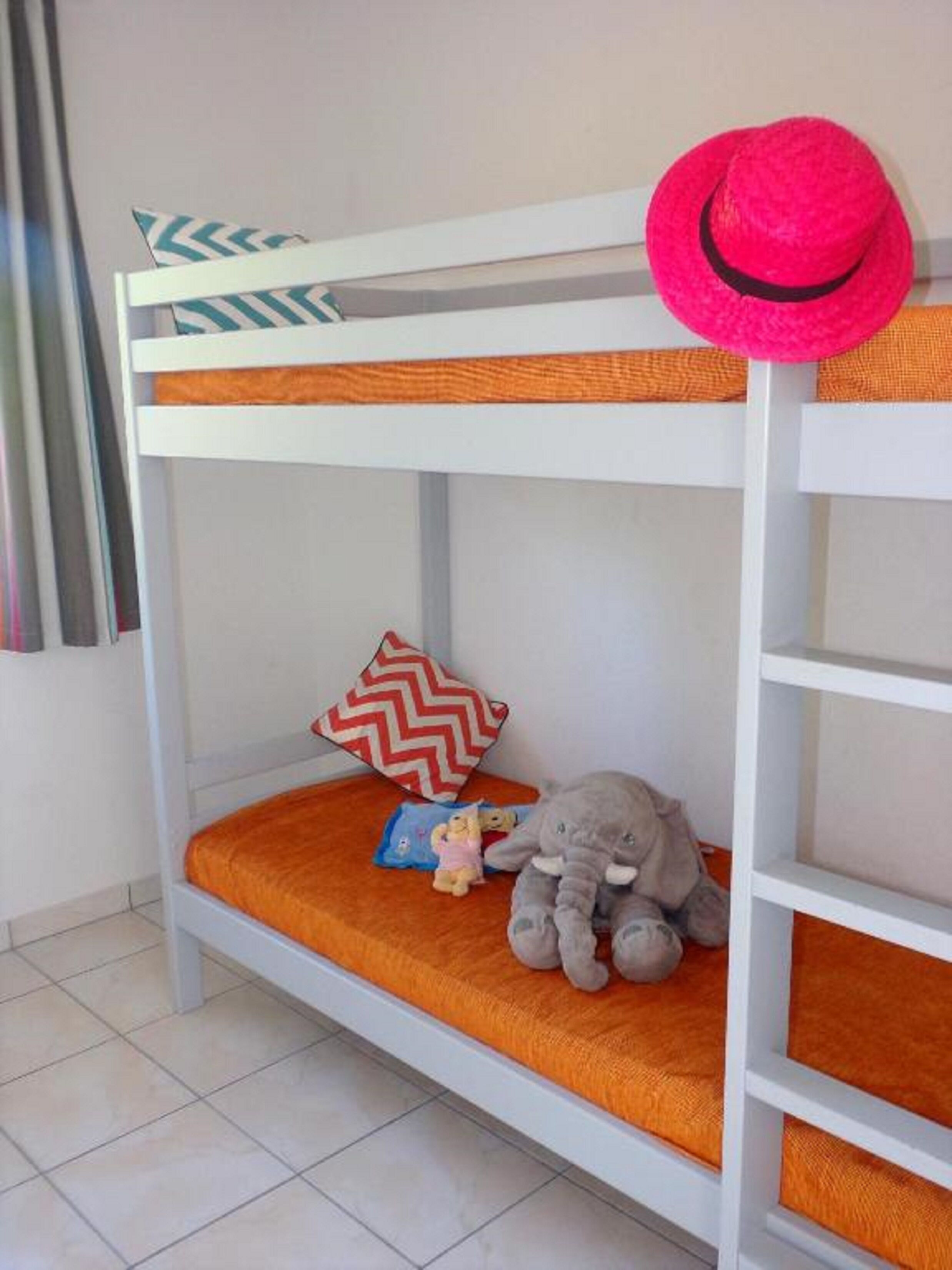 A bunk bed with an orange mattress, a red and white chevron pillow, and a stuffed elephant toy.