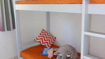A bunk bed with an orange mattress, a red and white chevron pillow, and a stuffed elephant toy.