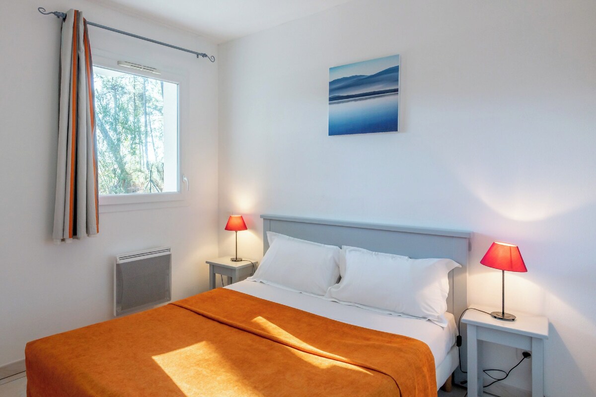 Une chambre à coucher avec un lit, deux tables de chevet avec des lampes, une fenêtre avec des rideaux, un radiateur et un tableau au mur.