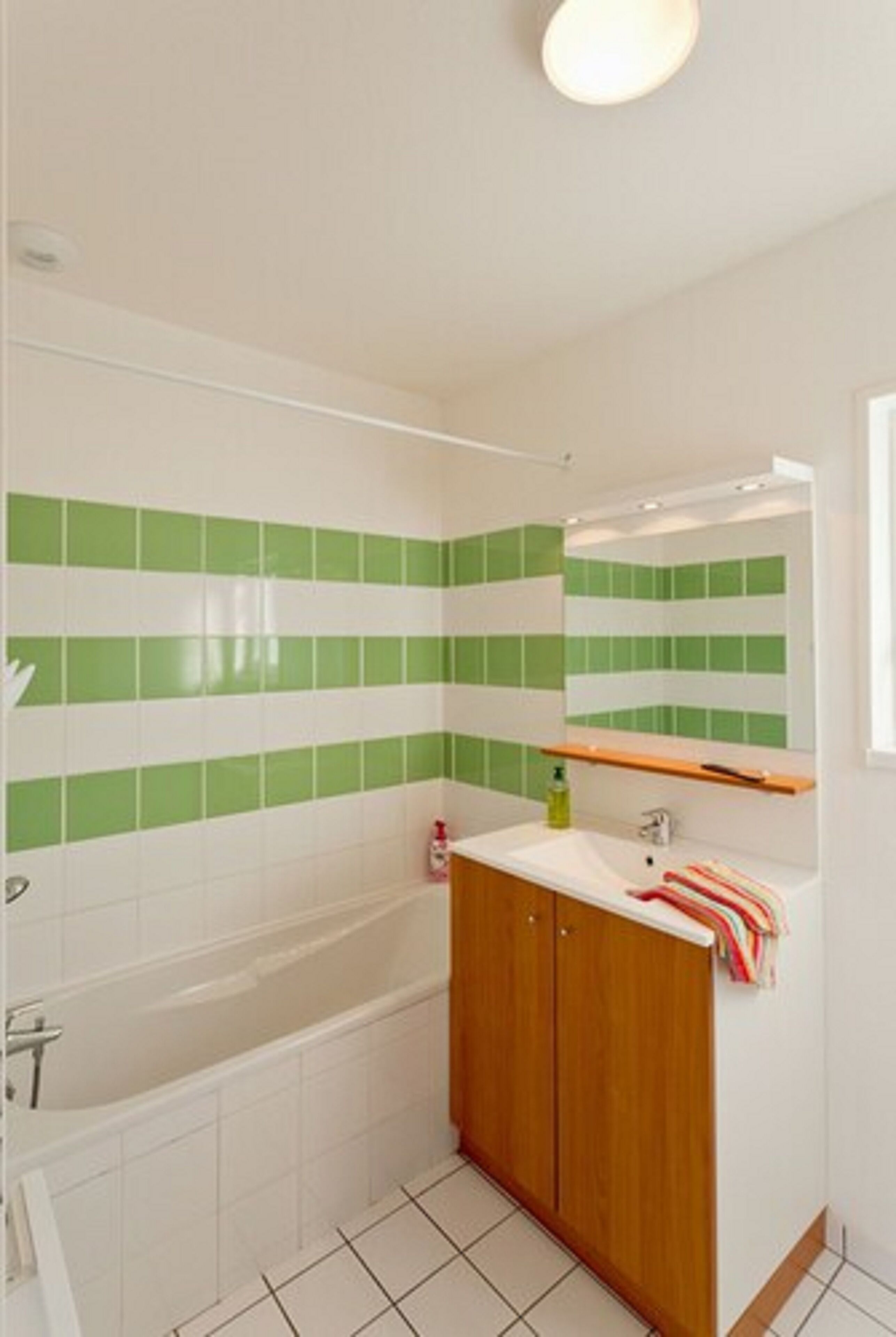 A bathroom with a bathtub, a wooden cabinet, a mirror, and green and white tiles.