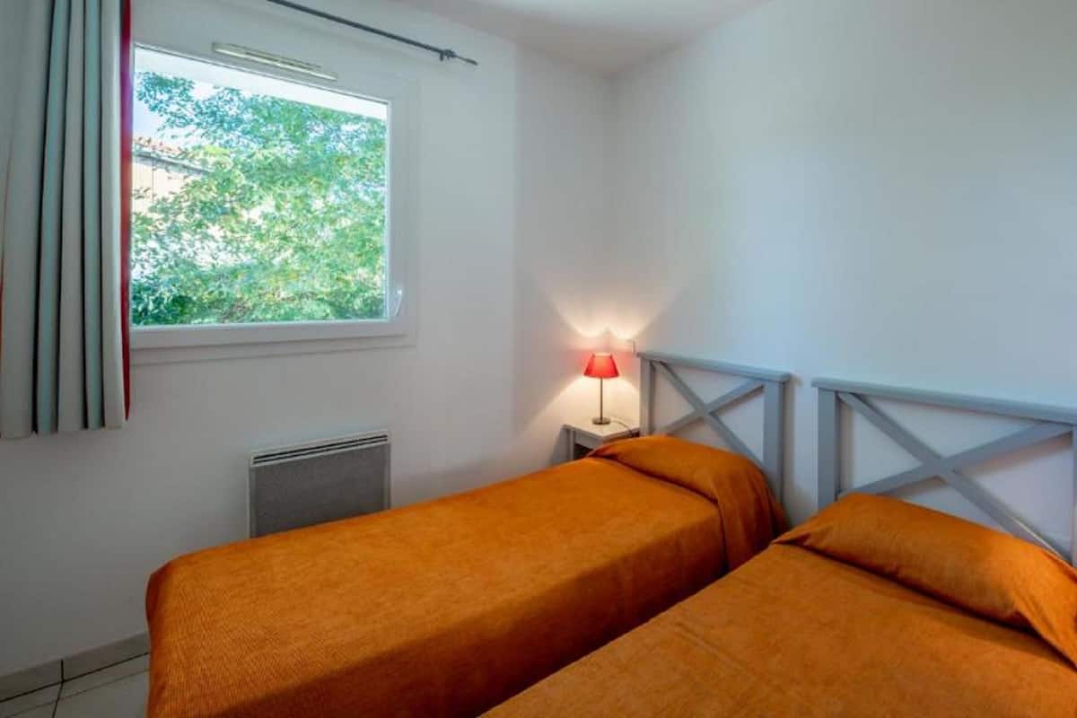 Una habitación con dos camas, una ventana con cortinas, un radiador y dos lámparas de noche.