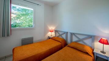 A room with two beds, a window with curtains, a radiator, and two bedside lamps.