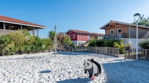 A sandy beach area with a playground structure, surrounded by residential buildings with red and brown exteriors. - Le Domaine des Grands Lacs - Vacancéole (Parentis-en-Born)