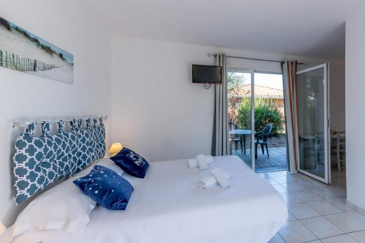 Un dormitorio con cama, almohadas, televisor y puerta corrediza de vidrio que da a un área exterior.