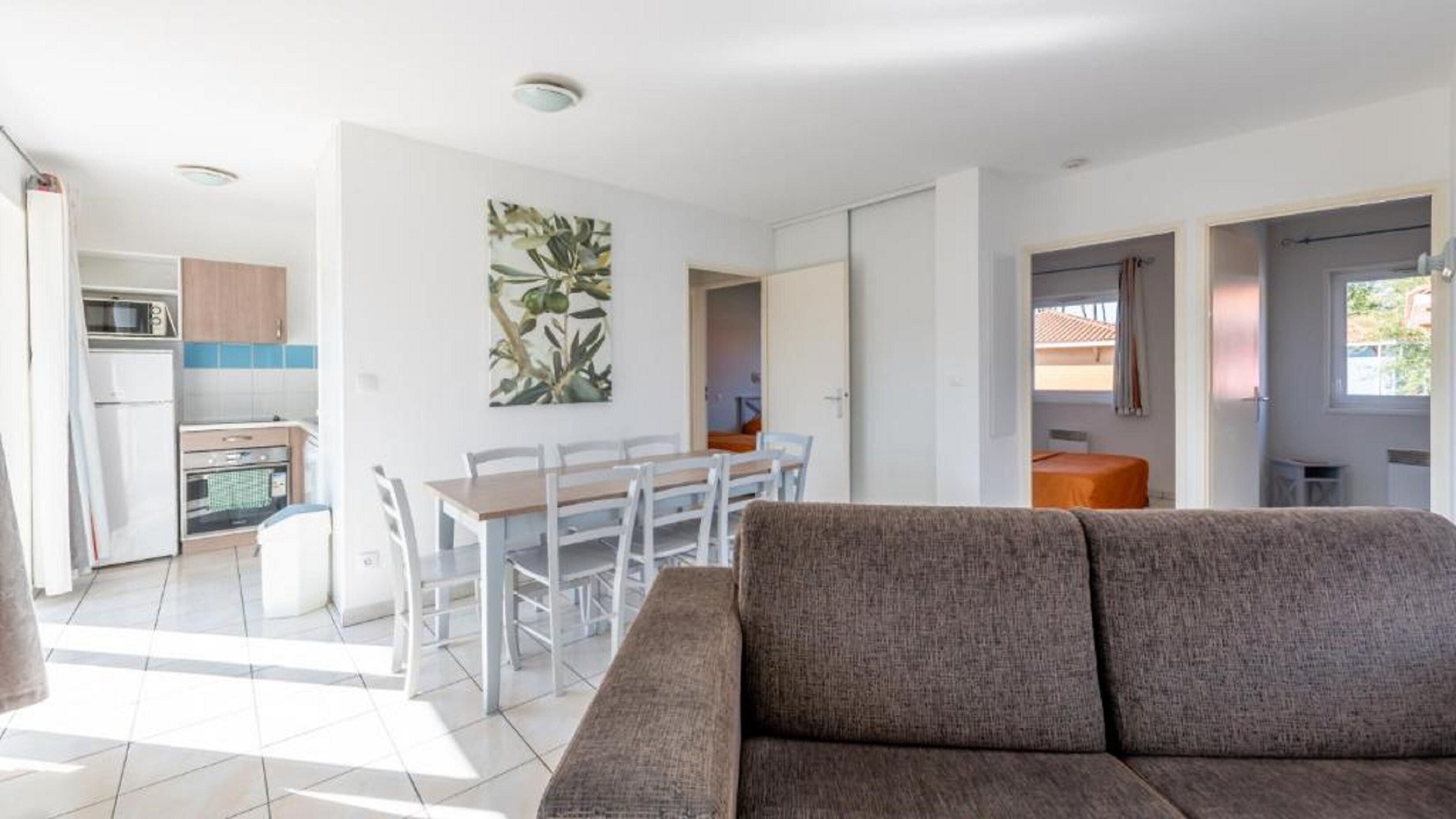 Una sala moderna con un sofá, un comedor con mesa y sillas, una cocina con armarios y electrodomésticos, y un ventanal grande que proporciona luz natural.