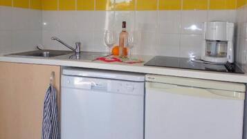 A compact kitchen with wooden cabinets, a white dishwasher, and a yellow-tiled backsplash.