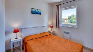 Quarto com uma cama, duas mesas de cabeceira, uma janela com cortinas, um radiador e um quadro pendurado na parede.