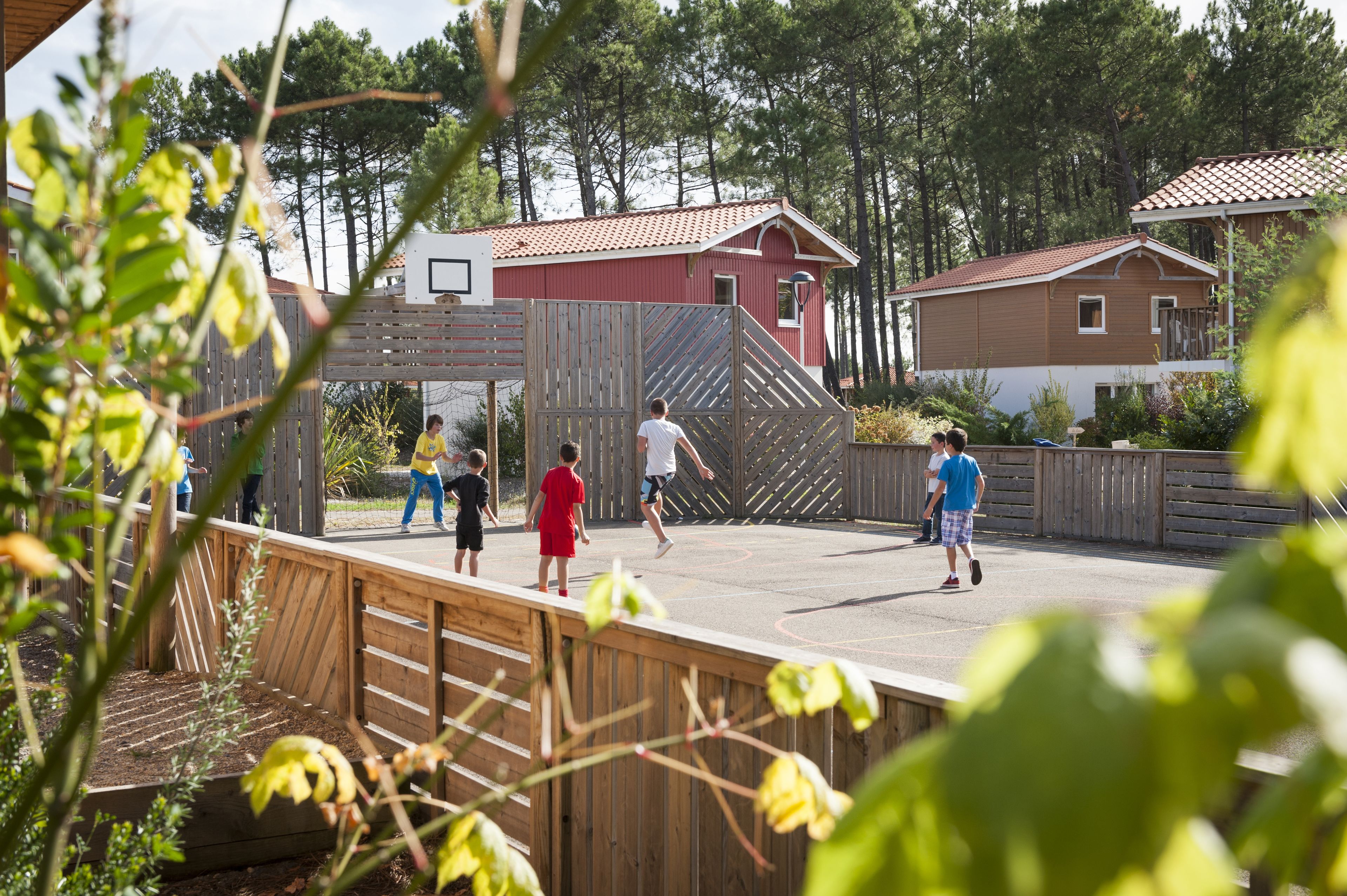 Un parque infantil con niños jugando, rodeado de vallas de madera y casas al fondo.