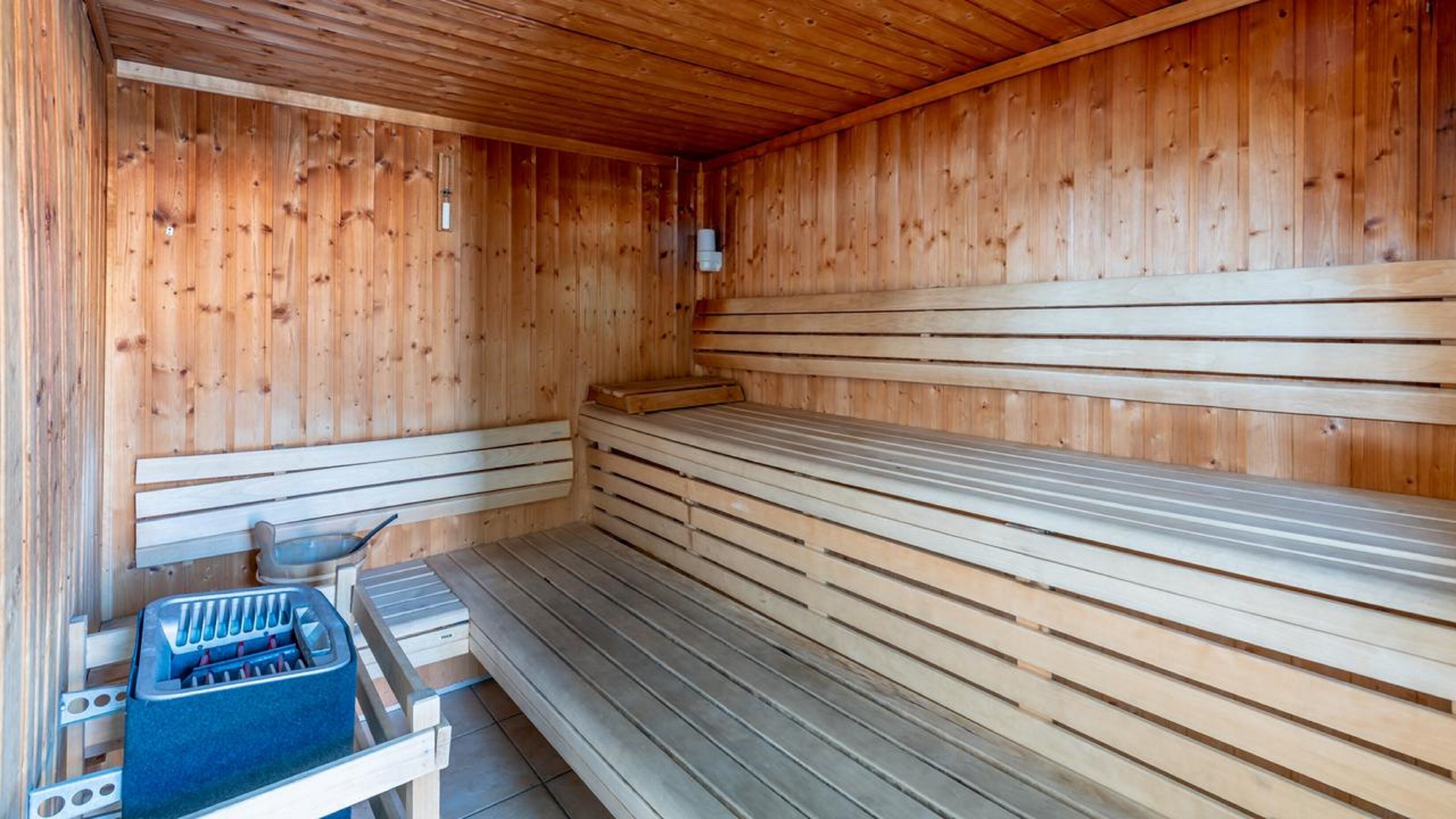 Un sauna avec des bancs en bois et une banquette, un banc muni d’un porte-serviettes et un banc avec un support à serviettes.