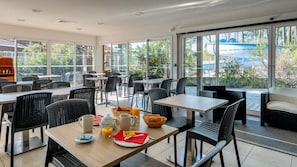 A modern dining area with tables and chairs, a breakfast setup with orange juice and pastries, and large windows offering a view of the outdoors. - Le Domaine des Grands Lacs - Vacancéole (Parentis-en-Born)