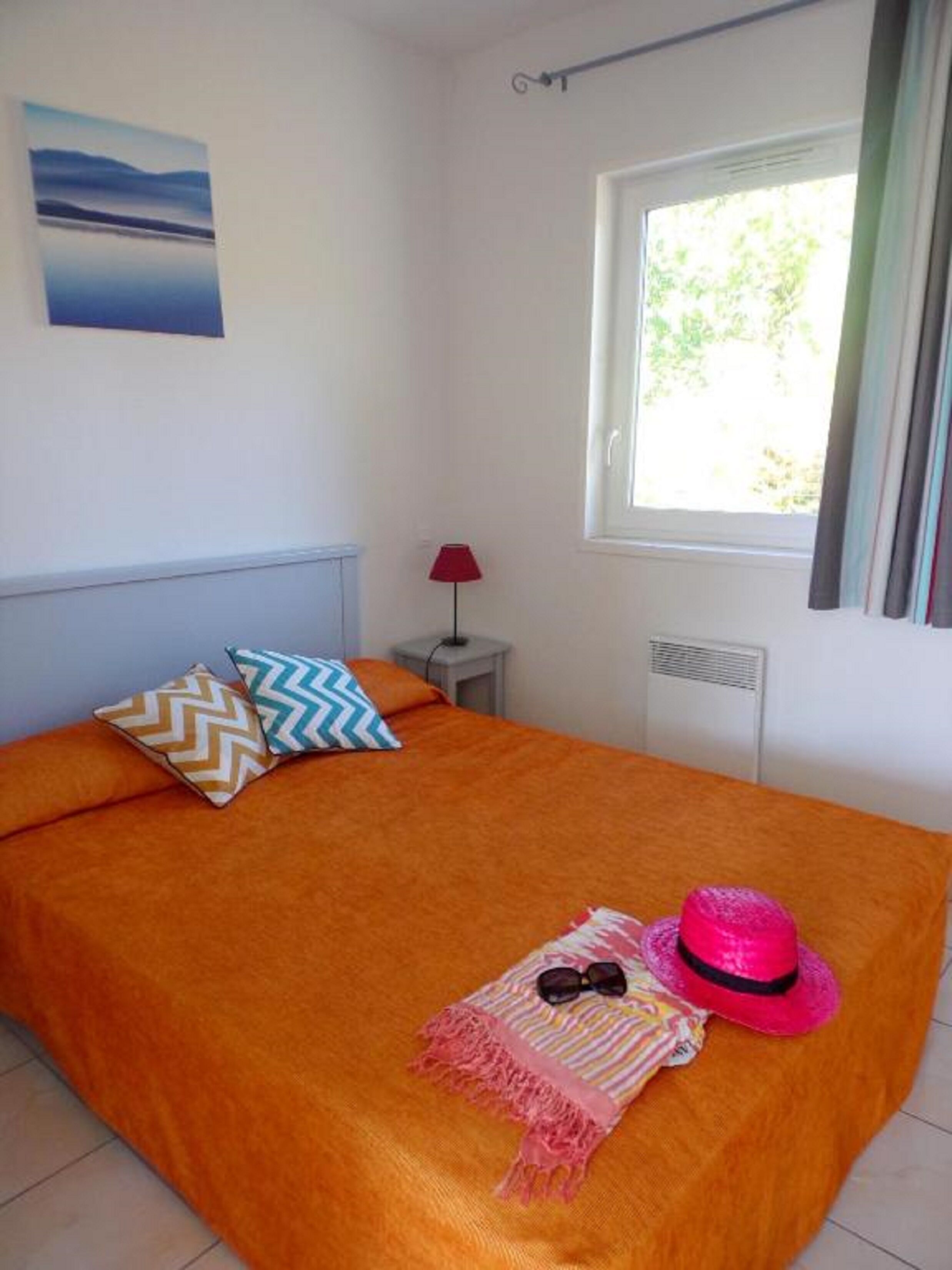 A bedroom with a large bed, a window with curtains, a lamp, and a painting on the wall.