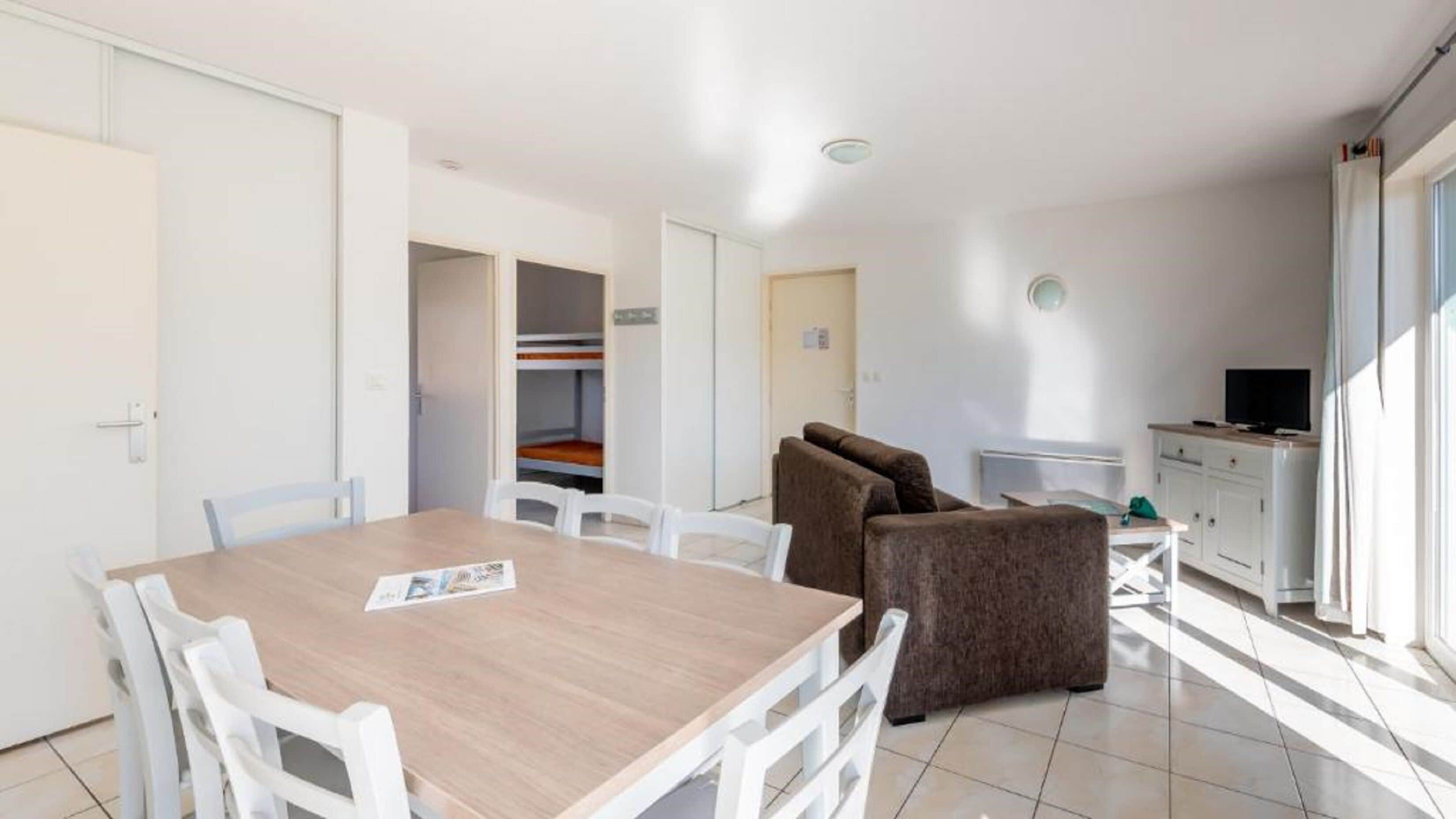 A compact living space with a dining area, a sofa, a television, and a kitchenette.
