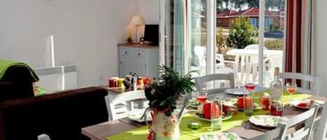 A dining area with a table set for four, surrounded by white chairs, a green table runner, and a potted plant.