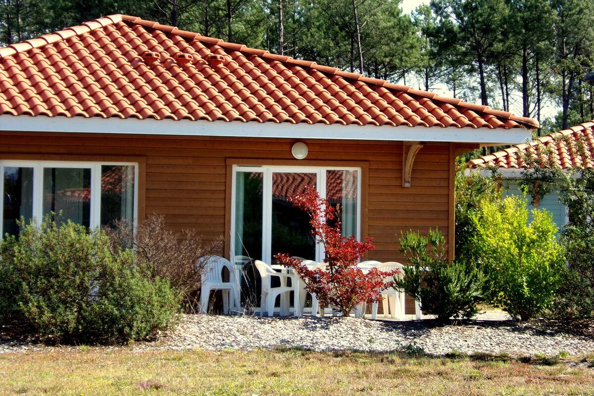 Una casa de madera con techo de tejas, un porche con sillas y un pequeño jardín.