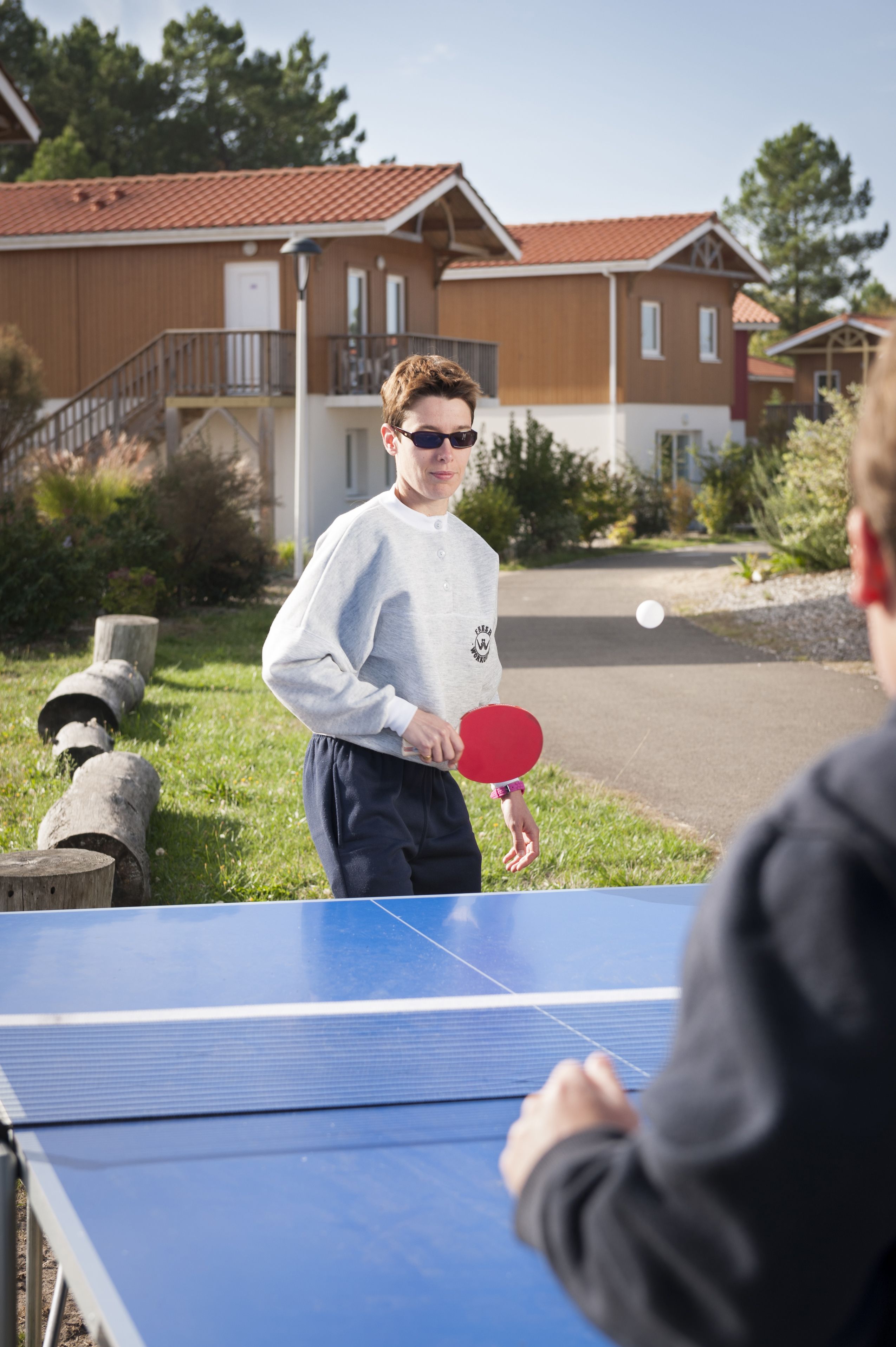 A person playing table tennis outdoors with a house in the background.
