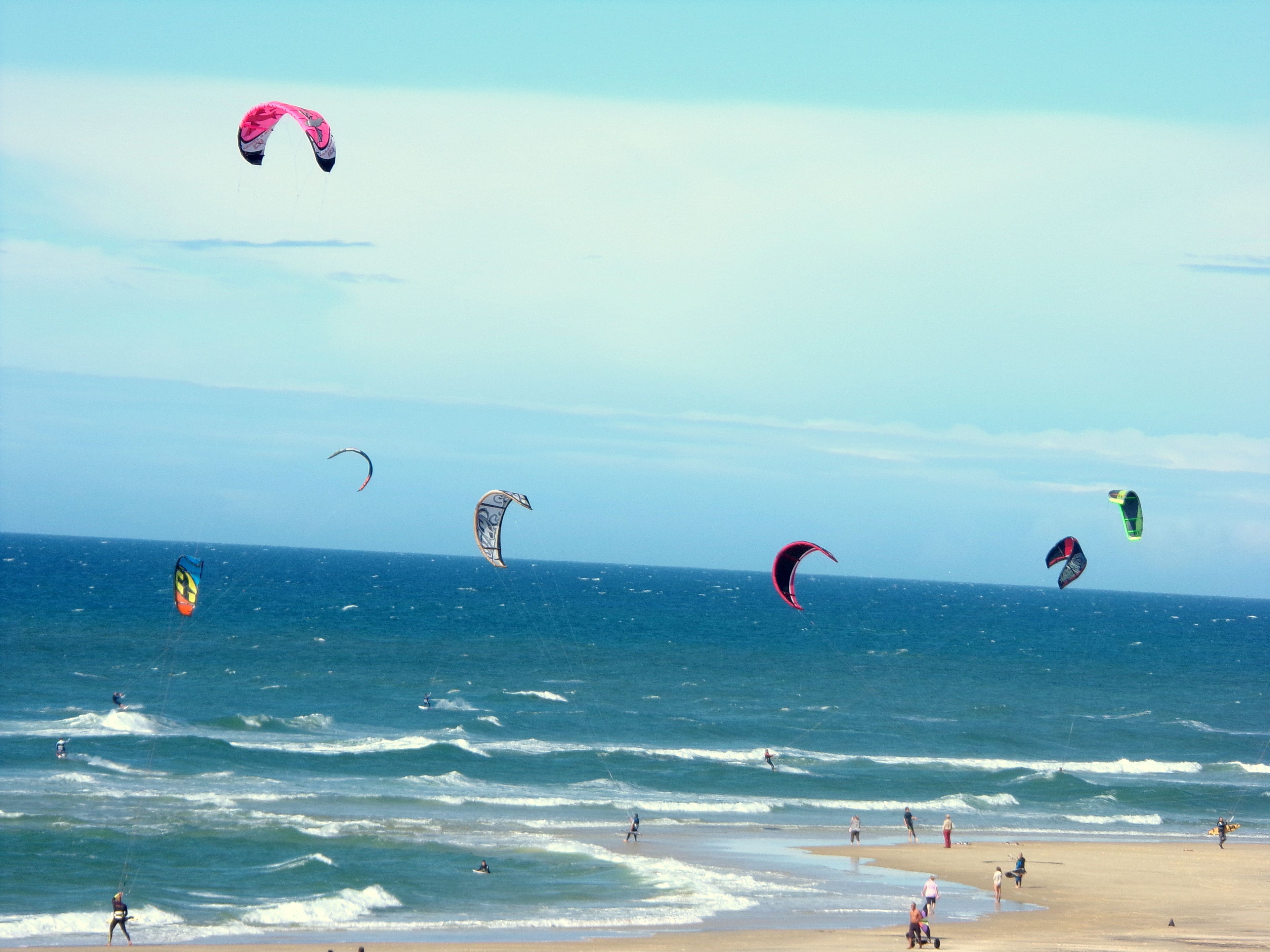 A beach with multiple kites flying over the water.