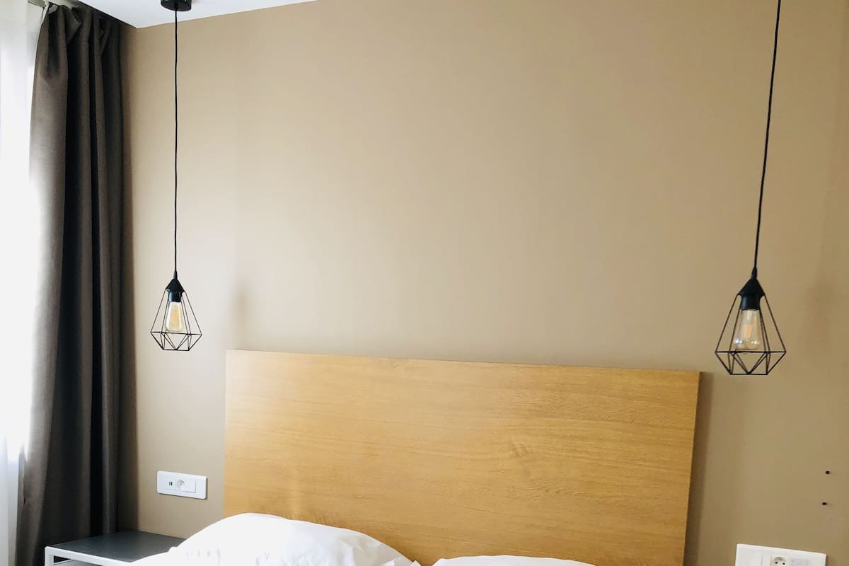 A hotel room with a large bed, two bedside tables, a wooden headboard, and two hanging light fixtures.