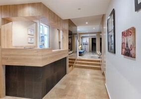 A reception area with a wooden reception desk, a staircase leading to a second floor, and a view of the Eiffel Tower through a window.