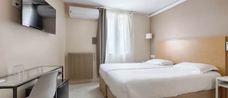 Habitación de hotel con cama, escritorio con silla, televisor montado en la pared y aire acondicionado.