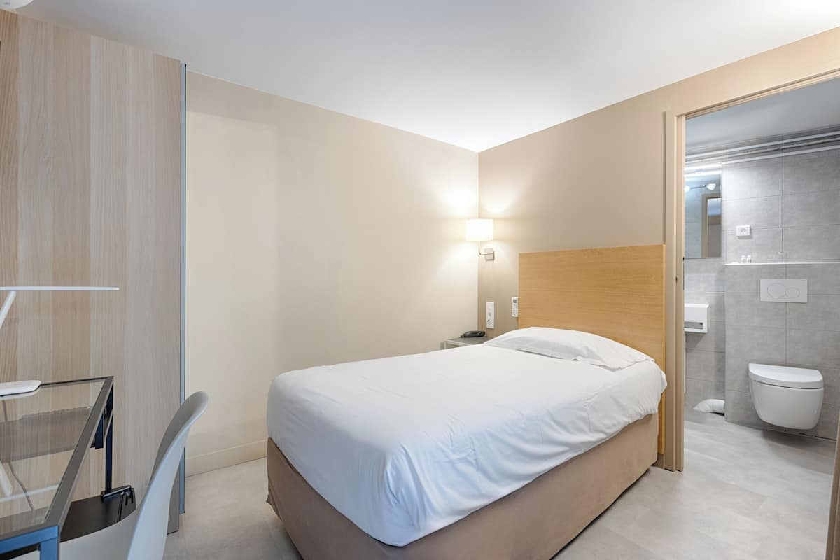 A modern hotel room with a bed, bedside table, and a glass desk.