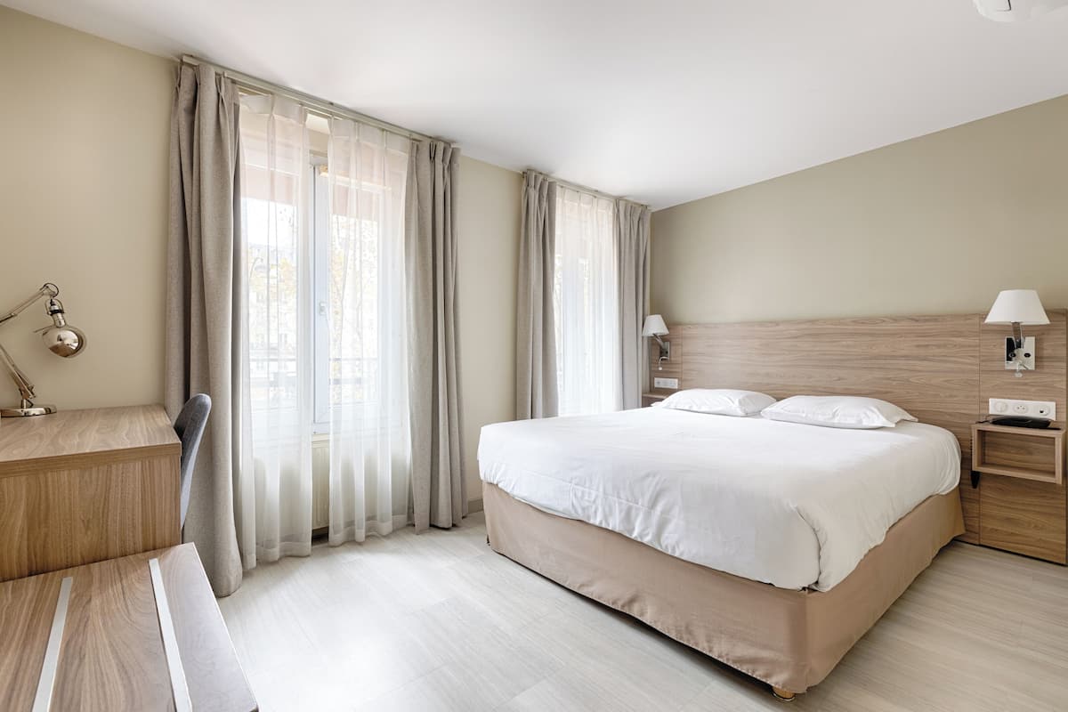 A hotel room with a large bed, a desk, and a chair.