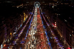 A nighttime cityscape with a Ferris wheel and a busy street lined with illuminated trees and street lamps.
