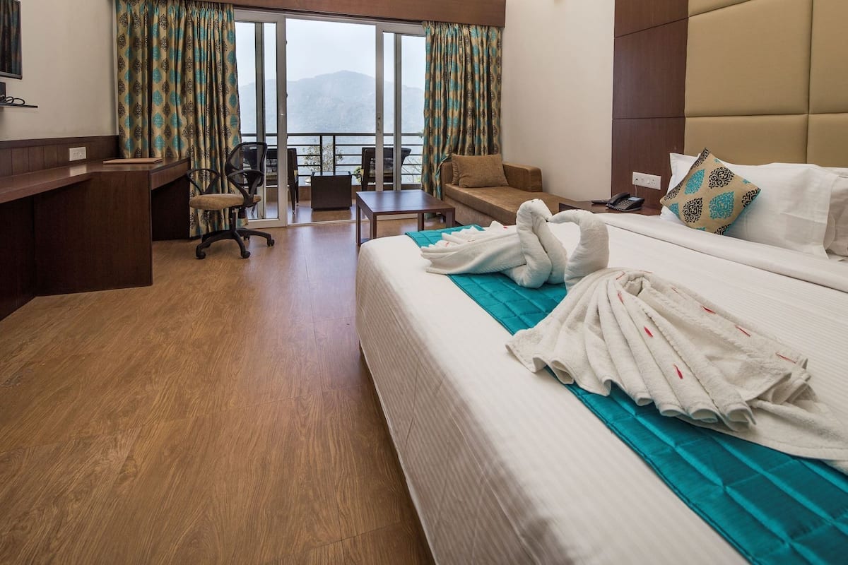 Une chambre d’hôtel équipée d’un lit, d’un bureau, d’une chaise, d’un canapé et offrant une vue sur les montagnes grâce à de grandes fenêtres.