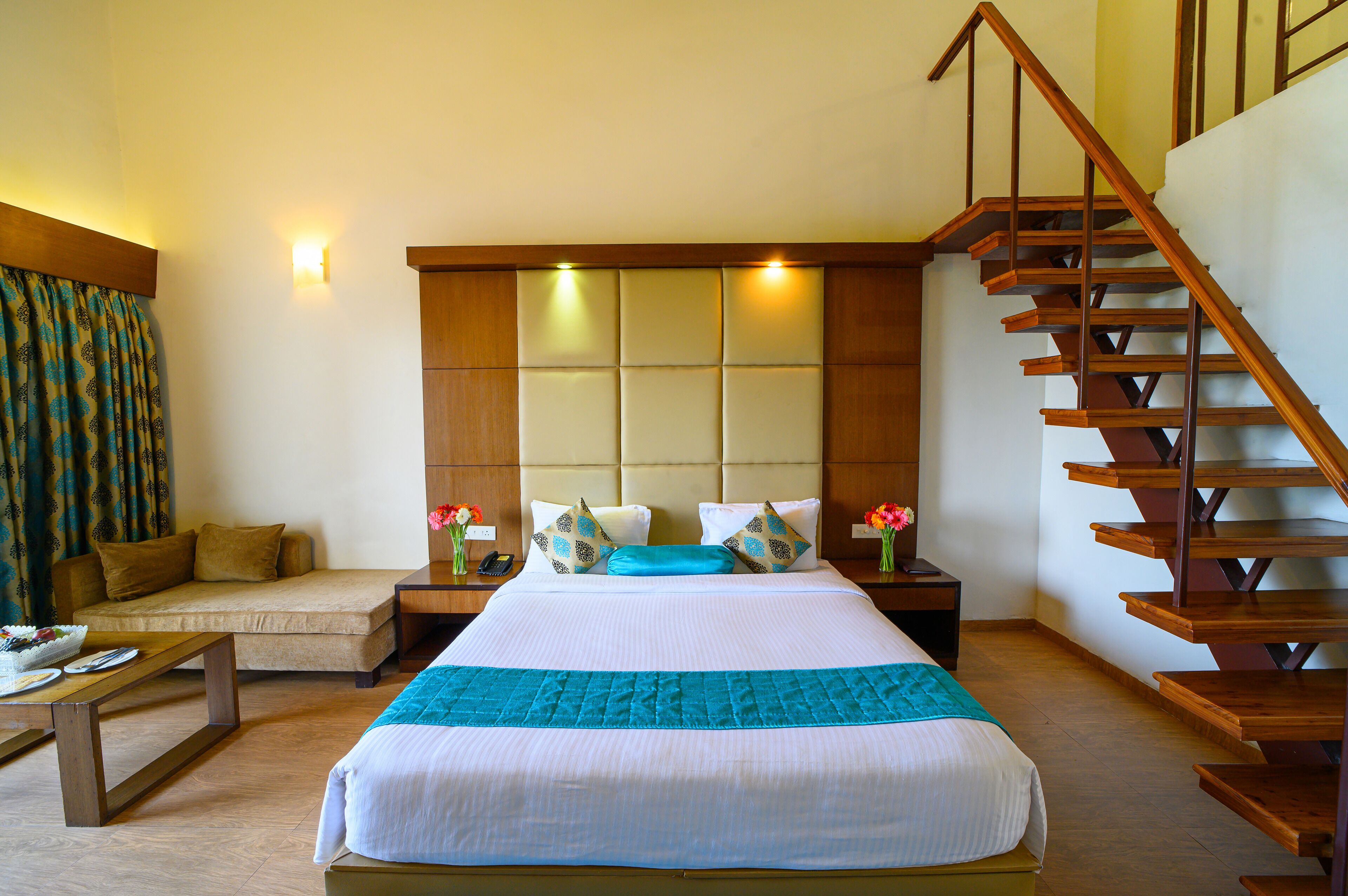 Ein Hotelzimmer mit einem großen Bett, einer Couch, einer Holztreppe und einem Nachttisch mit Lampe.