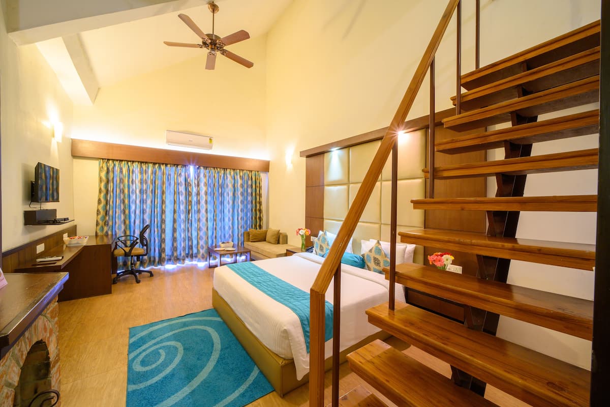 Une chambre d’hôtel avec un lit, un bureau, une chaise, un escalier en bois et un ventilateur de plafond.