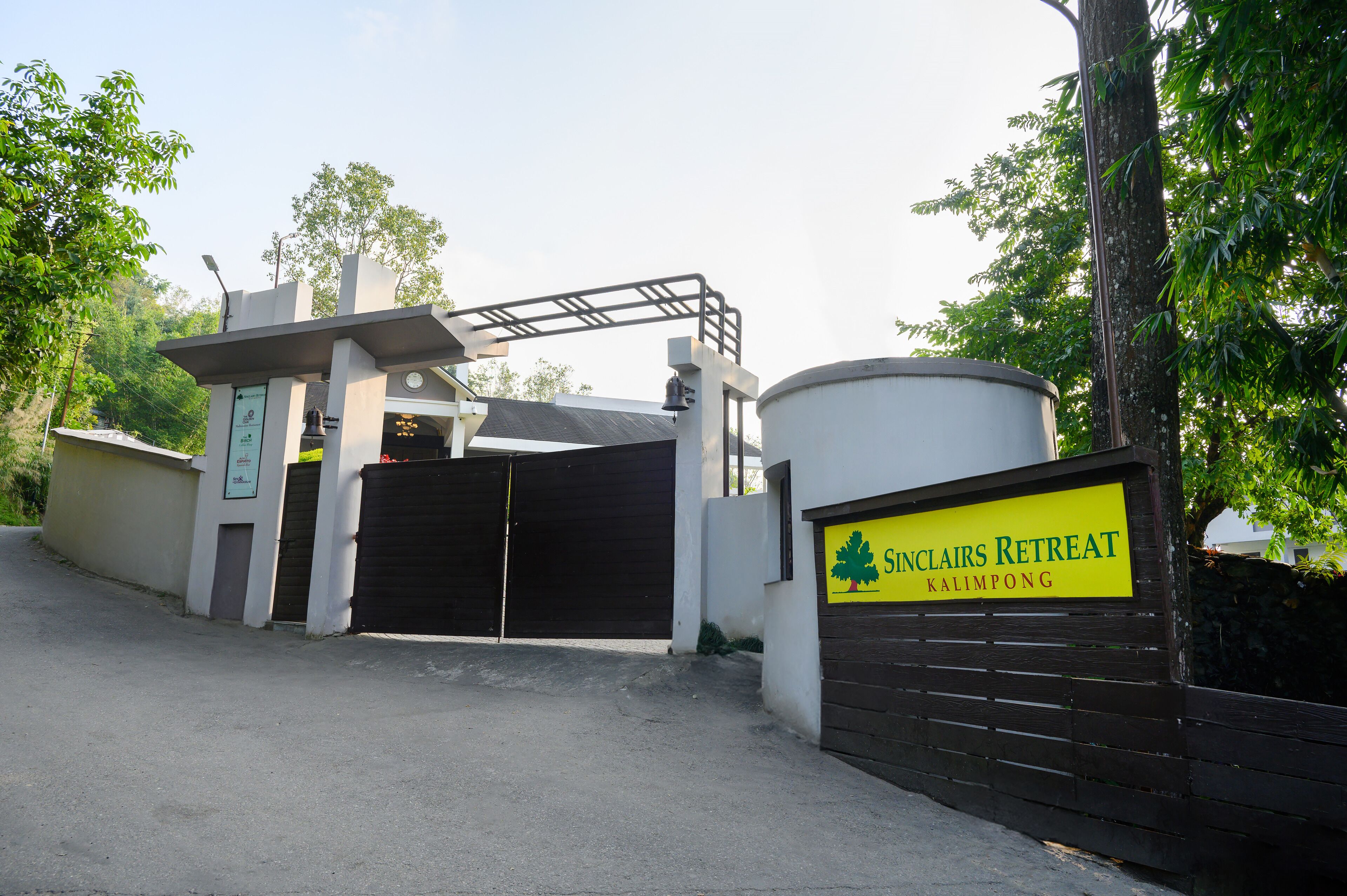 A gated entrance to a retreat named 'SincLairs Retreat Kalimpong' with a signboard, a bell, and a solar panel.