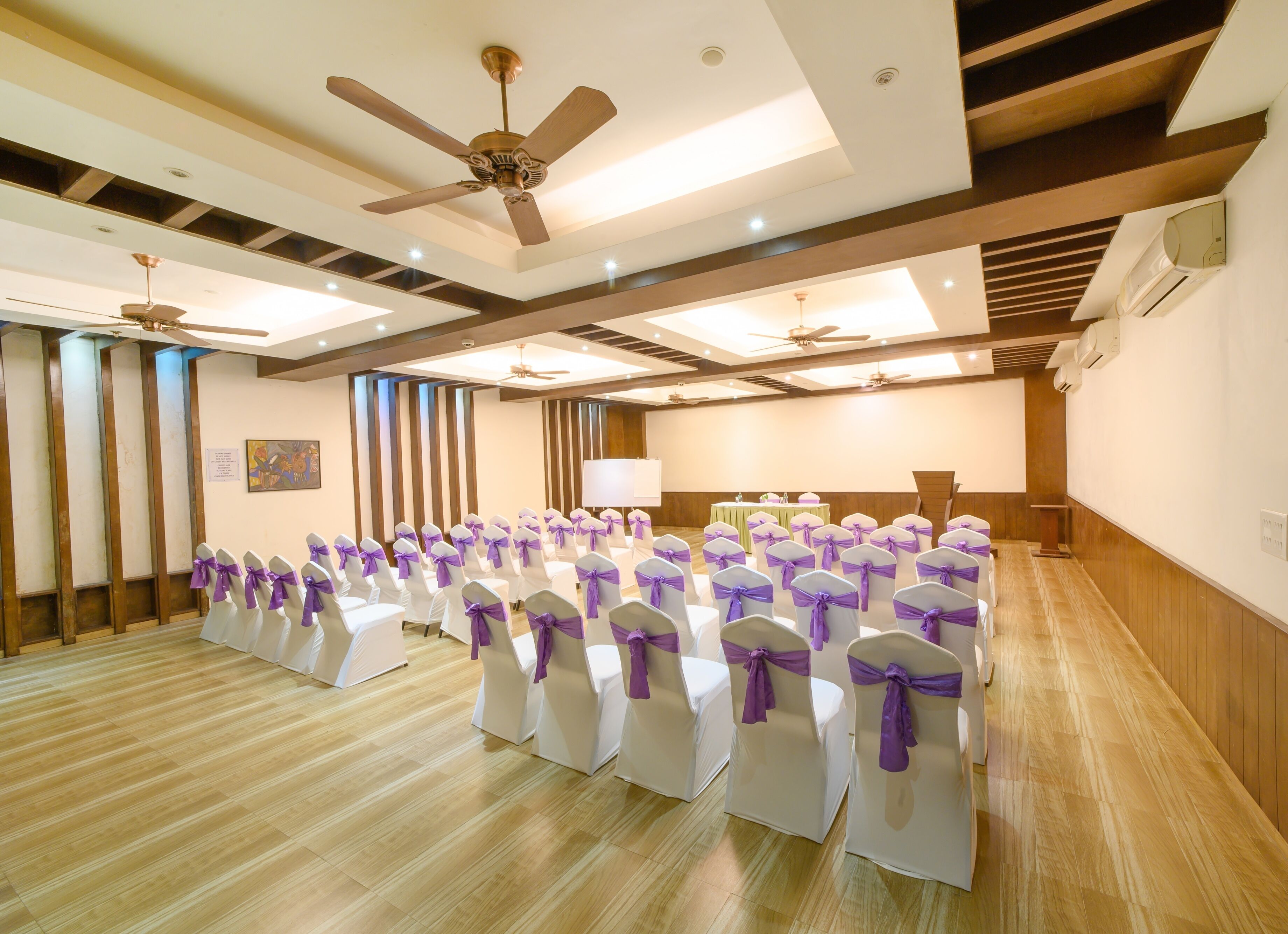 Ein Konferenzraum mit Reihen weißer Stühle mit violetten Bändern, Deckenventilatoren und einer Bühne.