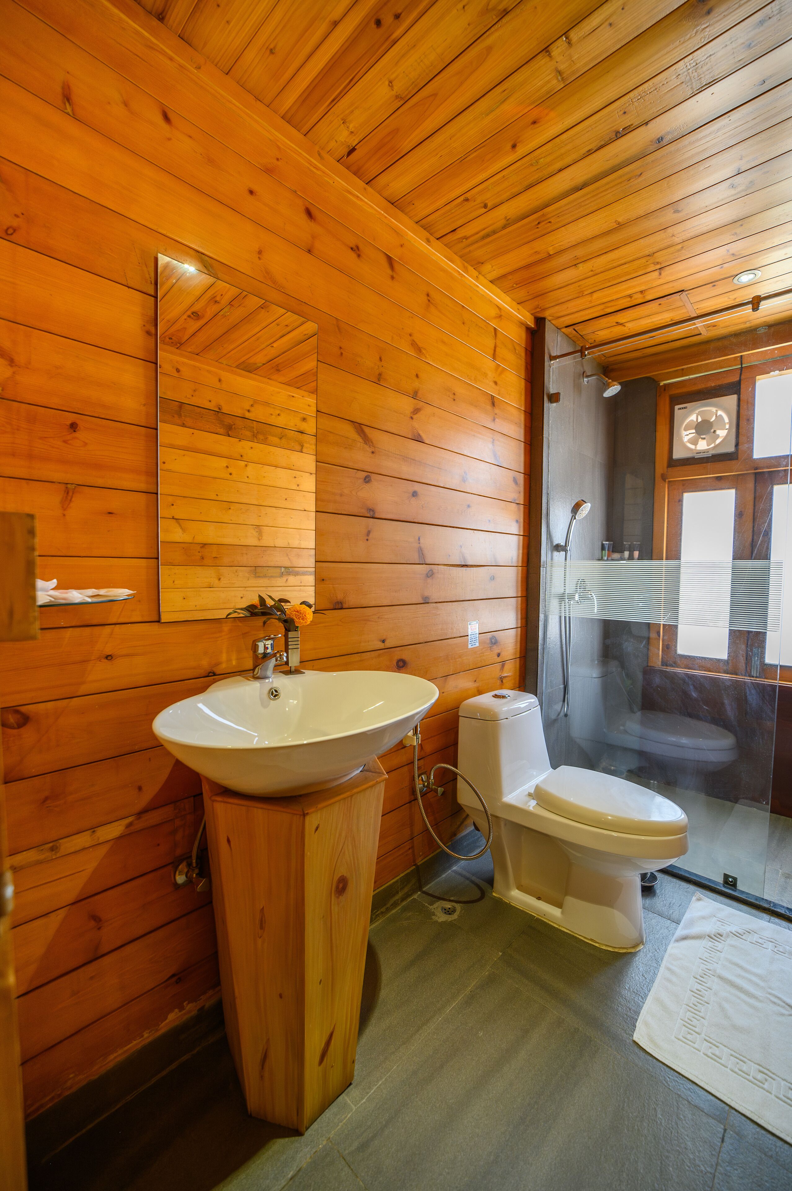 A wooden cabin bathroom with a sink, toilet, and glass-enclosed shower.