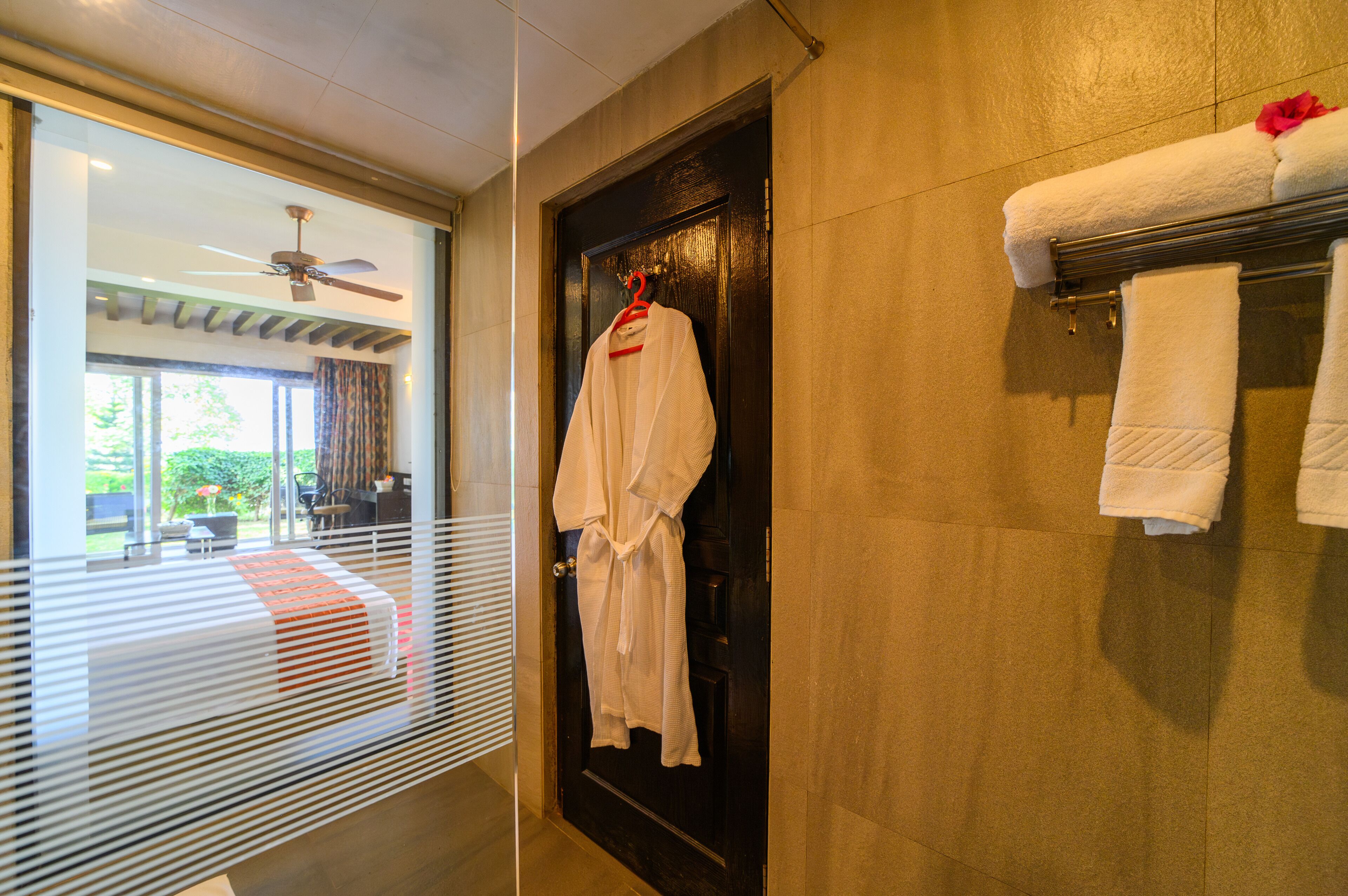 Habitación de hotel con una puerta de madera oscura, una bata blanca colgada en una percha y un perchero con dos toallas.