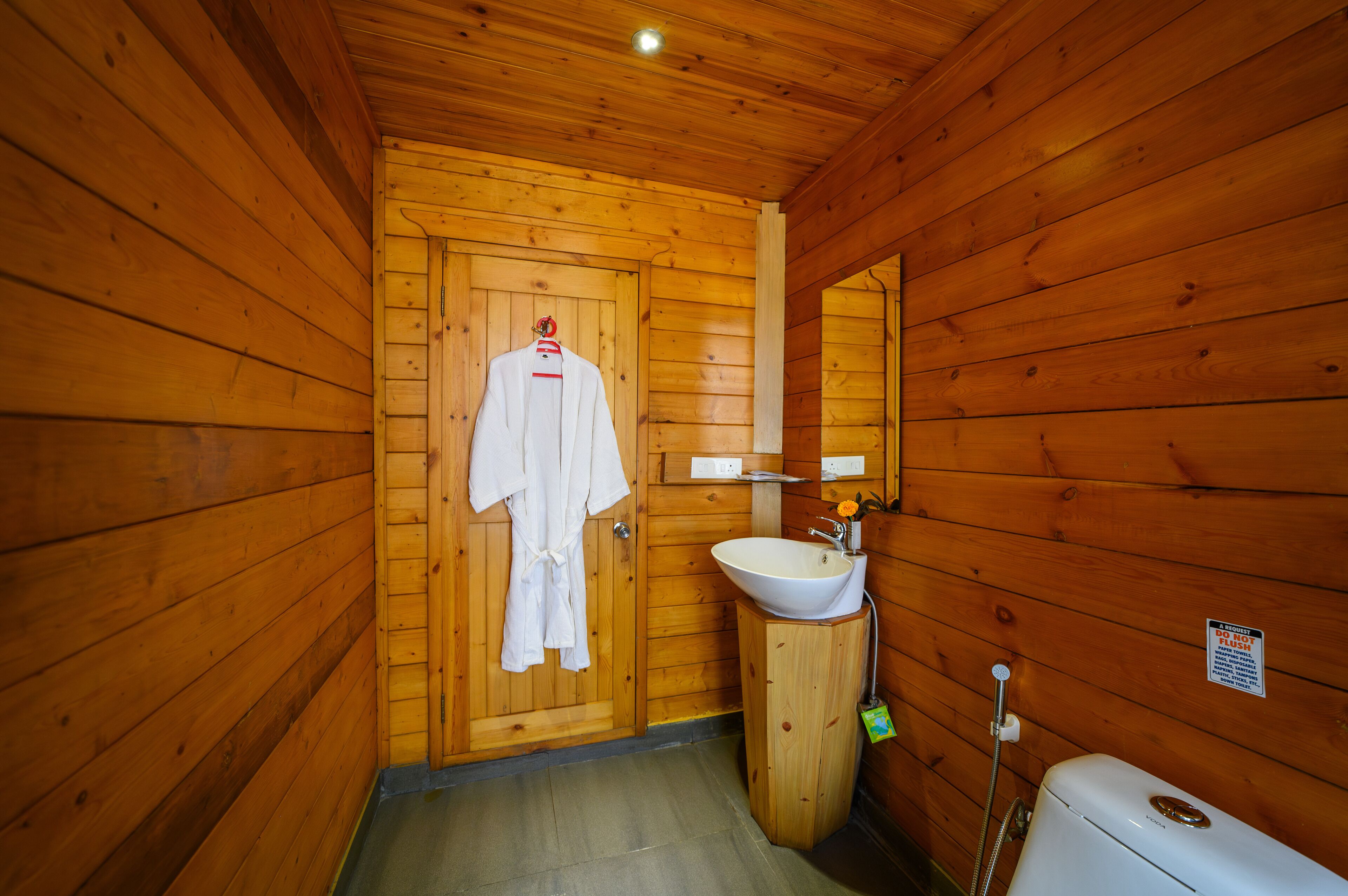 A wooden cabin bathroom with a wooden door, a white sink, and a toilet.