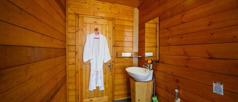 A wooden cabin bathroom with a wooden door, a white sink, and a toilet.