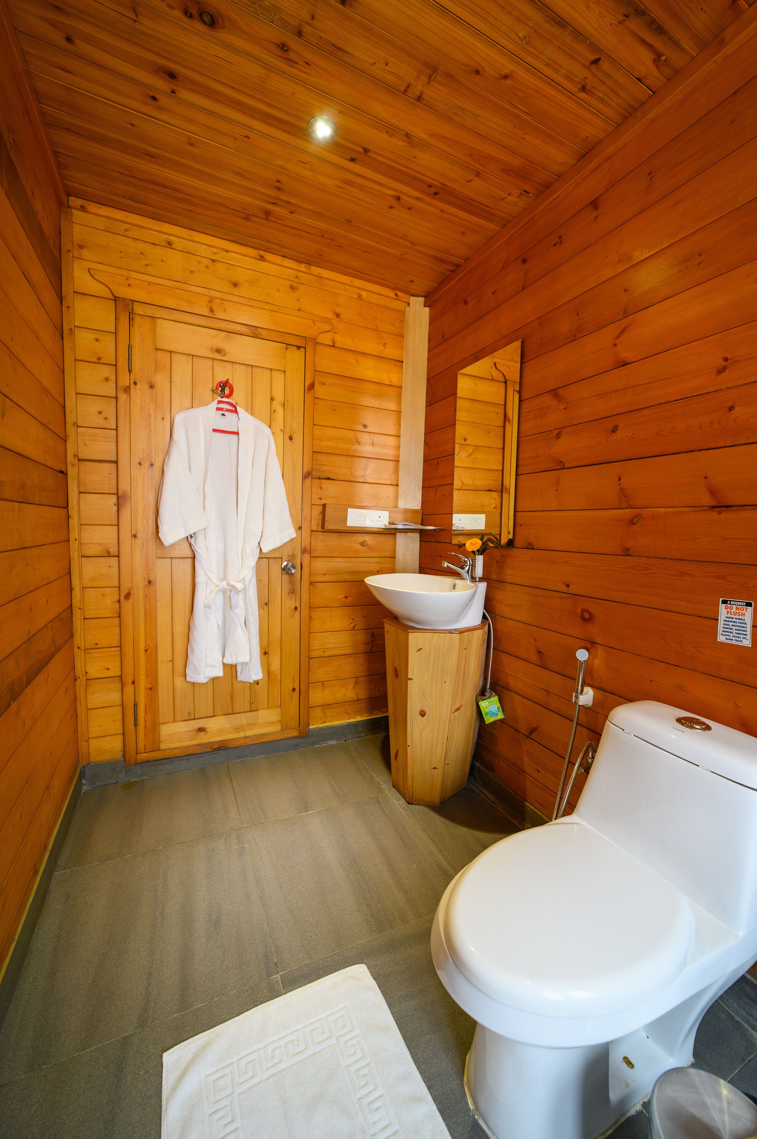 A wooden cabin bathroom with a wooden door, a white sink, a toilet, and a robe hanging on the door.