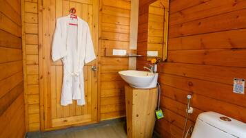 A wooden cabin bathroom with a wooden door, a white sink, a toilet, and a robe hanging on the door.
