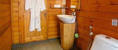 A wooden cabin bathroom with a wooden door, a white sink, a toilet, and a robe hanging on the door.