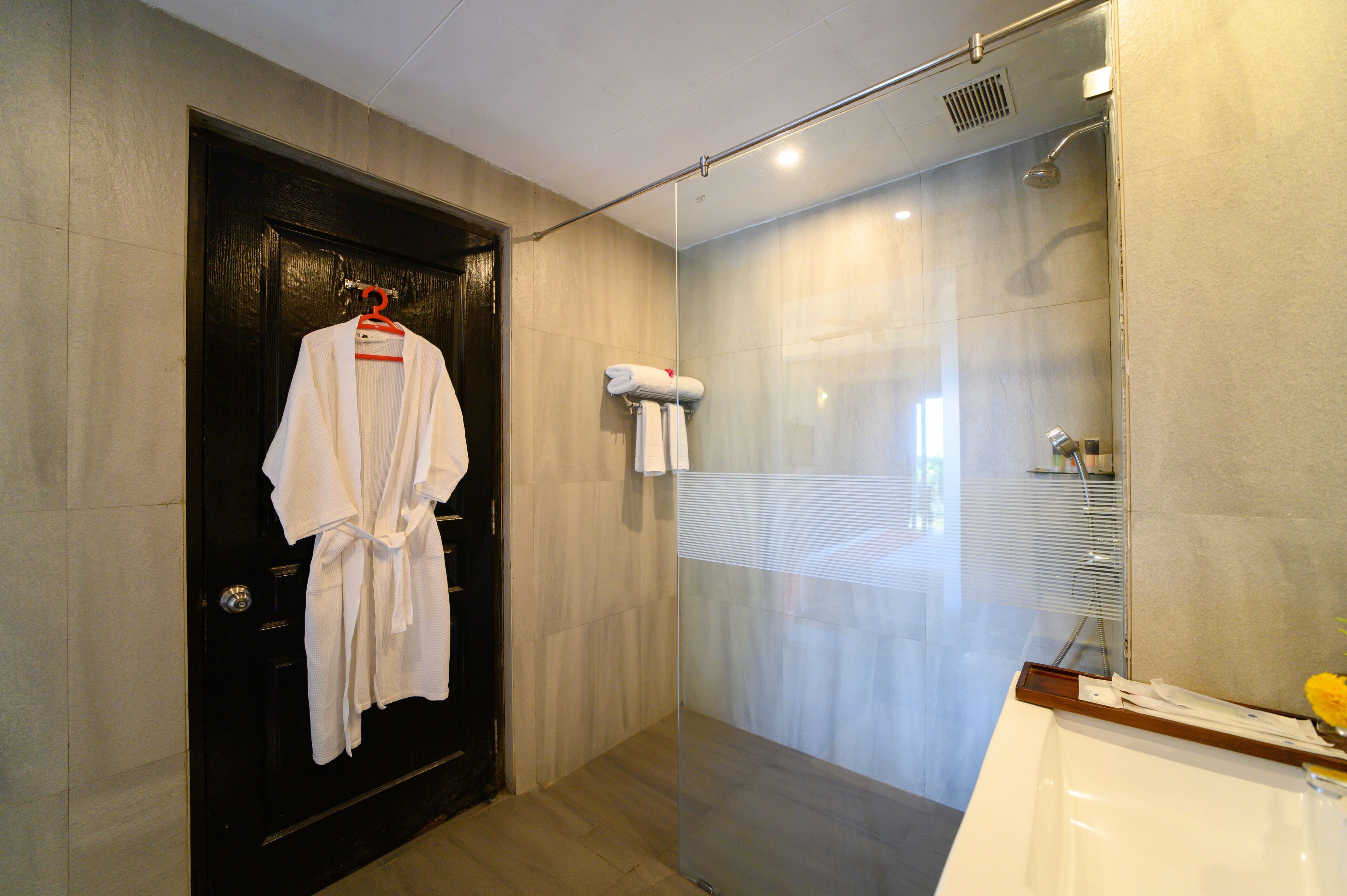 A bathroom with a black door, a white robe hanging on a red hanger, and a shower area with a glass partition.