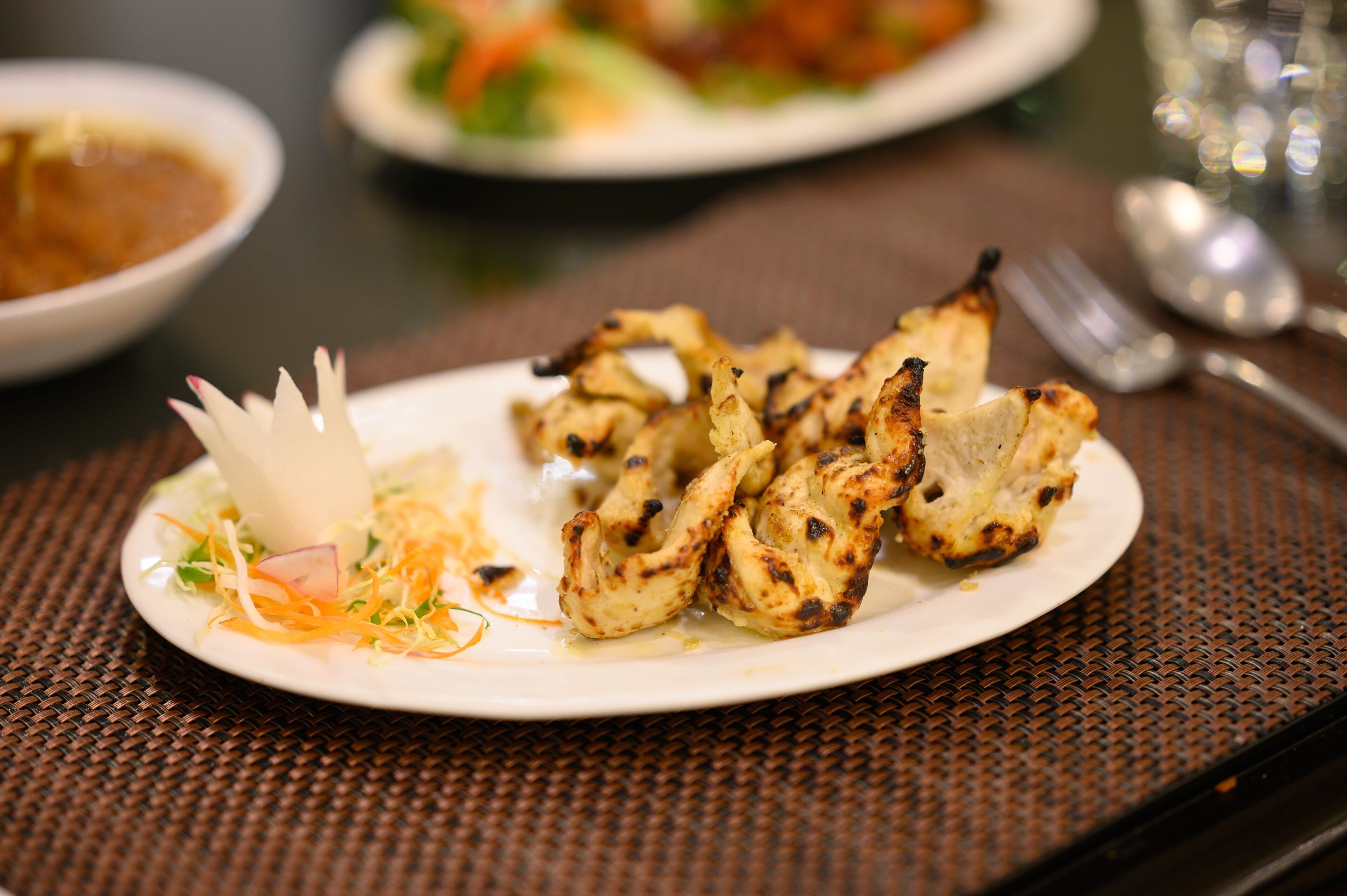 A plate of grilled chicken wings with a side of shredded vegetables and a decorative flower on a woven placemat.