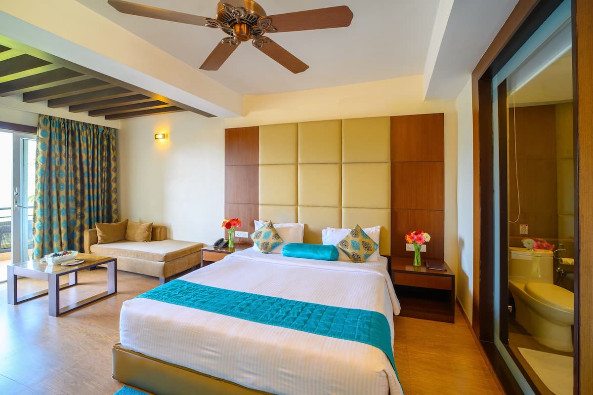 Une chambre d’hôtel moderne, dotée d’un grand lit, d’un canapé, d’une table basse et d’une salle de bain visible à travers une porte en verre.