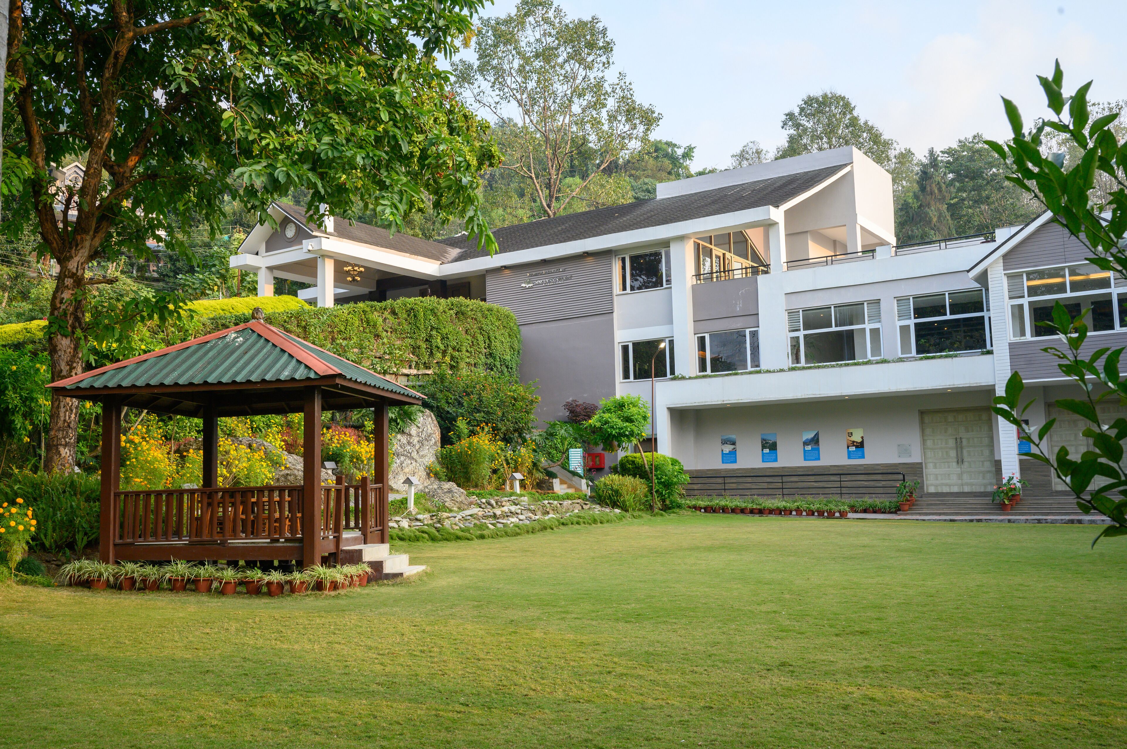 A modern house with a large lawn, a wooden gazebo, and a two-story structure with large windows.