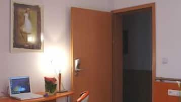 Een slaapkamer met een bed, een bureau met een laptop, een stoel en een deur.