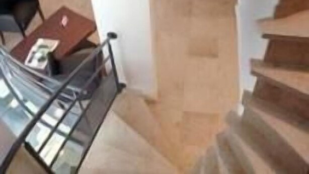 A modern interior with a staircase leading to an upper level, featuring a glass railing and a seating area below.